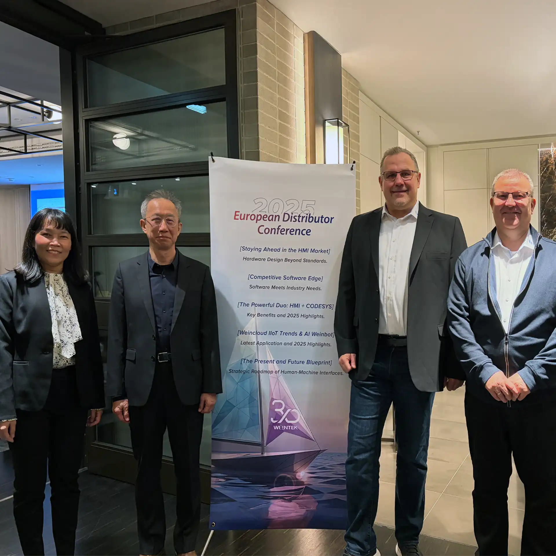 „Kate Lin, Sherman Hsieh, Frank Mömerzheim und Andreas Brück stehen neben einem Roll-up ‚2025 European Distributor Conference‘ in München.“